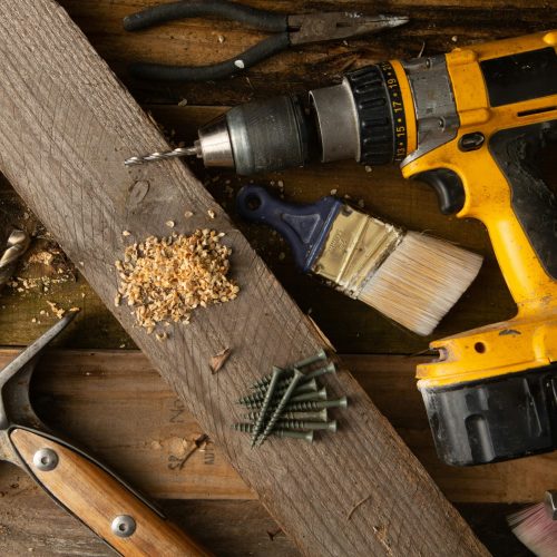A close-up of various tools including a drill, hammer, and paintbrush on a wooden workbench.